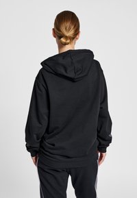 Svart hoodie med avslappnad passform, utrustad med stor huva och sänkta axlar. Materialet verkar mjukt, med ribbade muddar och fåll.