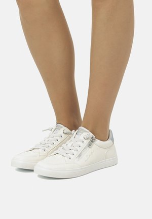 Zapatillas blancas con una textura suave, cierre de cordones, acentos plateados en el talón y detalle de cremallera en el lateral. Suela de goma, diseño de perfil bajo.