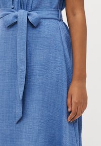 Rochie din in albastru, cu talie legată, având un material texturat, detalii cu nasturi și un design fluid.