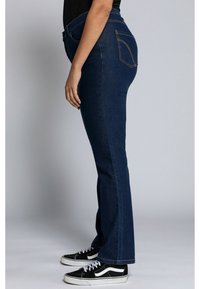 Jeans évasés en denim foncé avec une taille haute, des coutures verticales et deux poches arrière. Associés à des baskets noires et blanches.