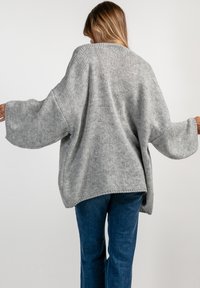 Oversized szary sweter dziewiarski o luźnym kroju, szerokich rękawach i strukturalnym wykończeniu, w połączeniu z niebieskimi dżinsami.