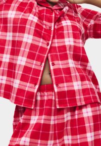 Rotes kariertes Flanell-Pyjama-Set mit einem knöpfbaren Oberteil mit Kragen, kurzen Ärmeln und passenden Shorts. Der Stoff wirkt weich und gemütlich.
