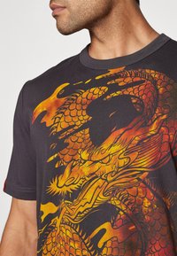 Camiseta negra de manga corta con un gran gráfico de dragón multicolor en rojo, naranja y amarillo, con intrincados patrones de escamas.