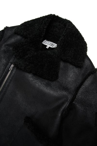 Jaqueta de couro preta com um colarinho de pelúcia preto, apresentando um fecho frontal e um acabamento suave e texturizado. Etiqueta visível no interior.