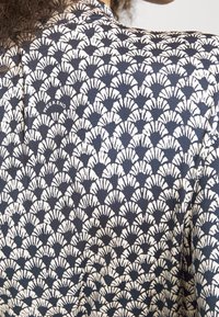 Personne portant une chemise bleu marine et blanche à motifs en forme d'éventail avec le mot "WEEKEND" imprimé près de l'épaule.