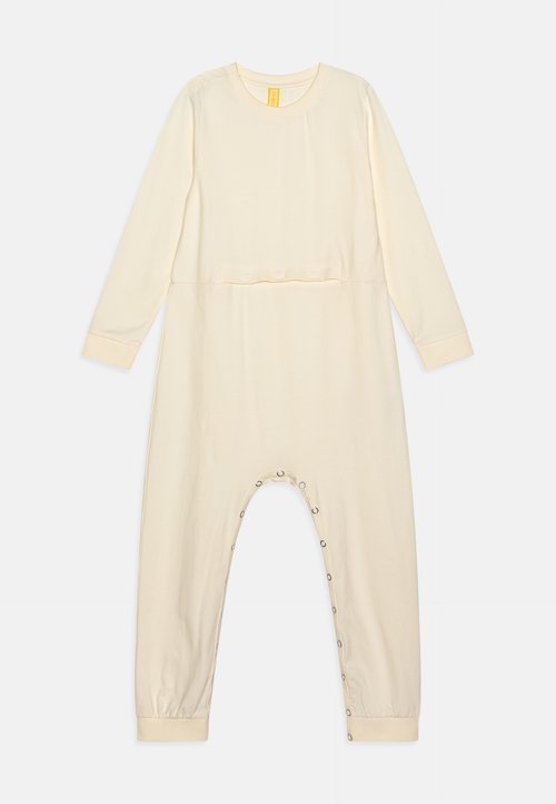 Combinaison longue à manches crème en tissu doux, avec un col rond, des fermetures à pressions le long de la jambe et des poignets ajustés.