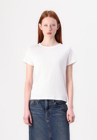 T-shirt bianco a maniche corte realizzato in tessuto a costine, con colletto rotondo e vestibilità dritta, abbinato a una gonna di jeans.
