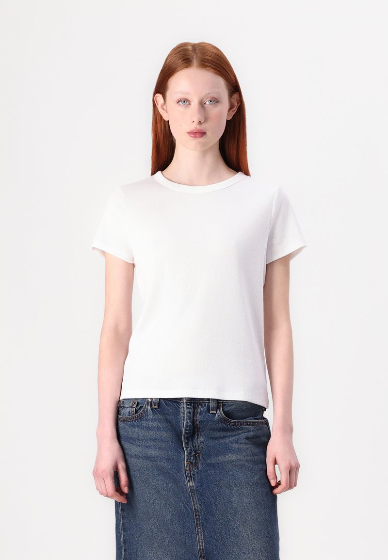 T-shirt bianco a maniche corte realizzato in tessuto a costine, con colletto rotondo e vestibilità dritta, abbinato a una gonna di jeans.