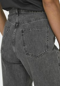 Jeans de cintura alta gris con un tejido de denim texturizado, que presentan dos bolsillos traseros y costuras de contraste a lo largo de las costuras.