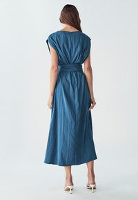 Maxi kleita teksturēta, tumši zila auduma ar īsām piedurknēm, izceltu vidukli un aizmugurējo rāvējslēdzēju. Pielāgota silueta ar plūstošu svārku.