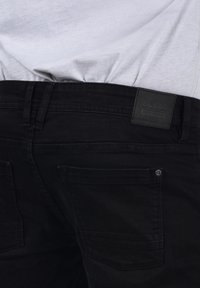 Černé džíny z denimu s texturovanou tkaninou, dvěma zadními kapsami a značkovou nášivkou na pasu. Design obsahuje akcenty v podobě švů.