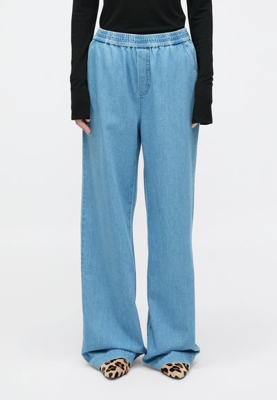 Pantaloni in denim azzurro chiaro a gamba larga con vita elastica e tasche laterali, abbinati a una maglietta a maniche lunghe nera e scarpe con stampa leopardo.