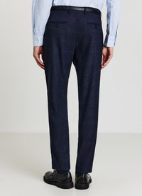 Dunkelblaue Anzughose mit strukturiertem Muster, geradem Schnitt und doppelten Gesäßtaschen. Kombiniert mit schwarzen Schuhen und einem hellblauen Hemd.