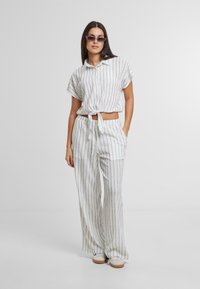 Set di due pezzi bianco realizzato in tessuto leggero, caratterizzato da strisce verticali nere. La parte superiore ha maniche corte e un dettaglio con nodo, mentre i pantaloni sono a gamba larga.