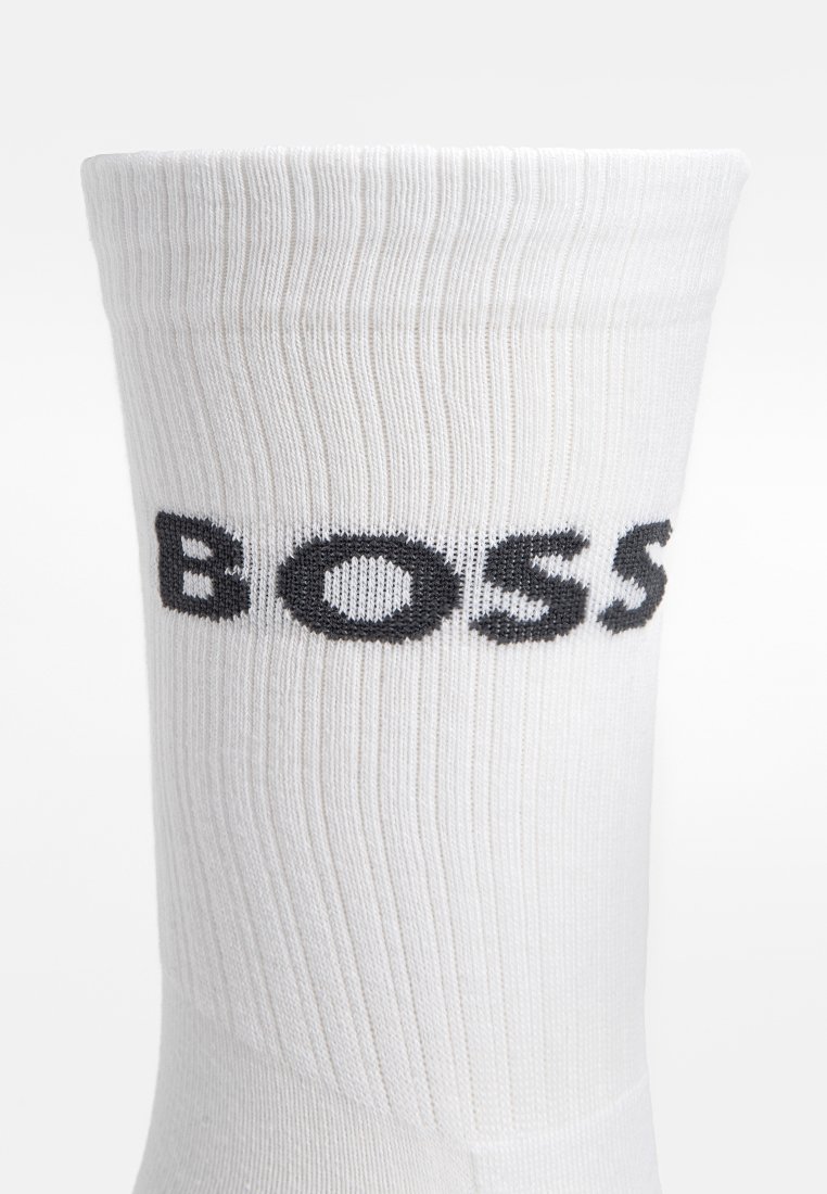 Weißes Baumwollsocken mit gerippter Textur, das ein auffälliges schwarzes "BOSS"-Logo nahe der Oberseite zeigt. Das Design ist schlicht und unauffällig.