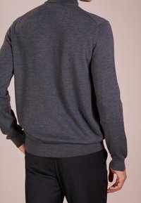 Gråstickad tröja med hög krage och långa ärmar. Tyget verkar slätt med en lätt glans. Har ribbade muddarna och nedre fållen.