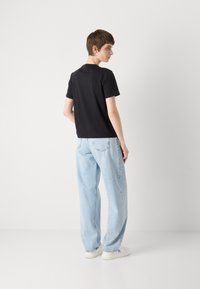 Zwarte korte mouwen T-shirt in combinatie met lichtblauwe wijde jeans en witte sneakers. Glad materiaal, eenvoudig ontwerp en een comfortabele pasvorm.