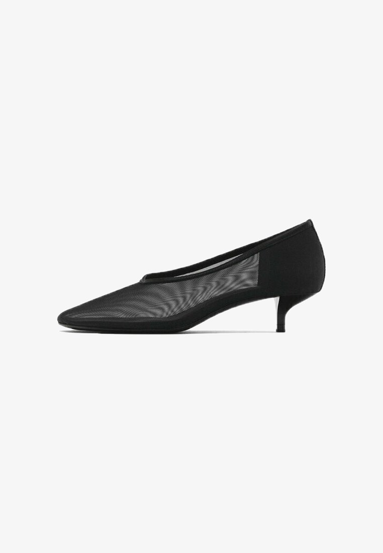 Escarpin féminin noir à bout pointu avec un petit talon kitten et des côtés en maille transparente sur fond blanc.
