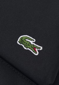 Tela negra con superficie texturizada, que presenta un logo de cocodrilo verde contorneado en blanco y acentuado con detalles rojos en la boca.