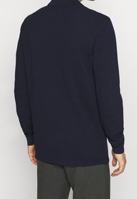 Námořnicky modrý polo tričko s dlouhými rukávy a límečkem, se uvolněným střihem a pružnými manžetami, vyrobené z měkké bavlněné látky.