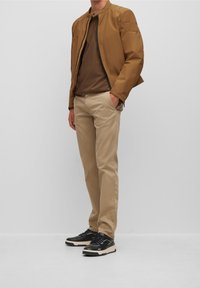 Khaki chinos, hnědé tričko a svetrová bundička světle hnědé barvy. Texturovaná tkanina, žebrovaný límec, zip a kontrastní černé tenisky.