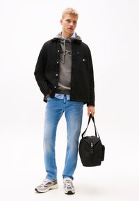 Must värviline jakk halli kapuutsiga, millel on tekst "Tommy Jeans", helesinised teksad, hallid ja valged tossud ning must kott.