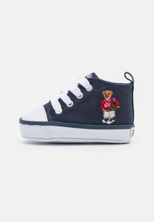 Granatowy sneaker dla malucha z białymi sznurowadłami i podeszwą, z wyszywanym misiem w czerwonym swetrze trzymającym piłkę do koszykówki z boku.