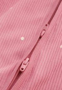 Närbild av ett rosa ribbat tyg med små vita prickar och en matchande rosa dragkedja delvis stängd.