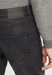 Vaqueros de denim negro con una cinturilla texturizada, detalles de desgaste y un bolsillo trasero con un diseño único de costura en ángulo.
