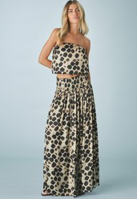 Haut sans bretelles raccourci et jupe longue en tissu beige avec un motif à pois noirs. La jupe présente une taille élastique et un design plissé.