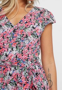 Abito floreale con sfondo nero e fiori rosa, bianchi e blu, scollatura a V, maniche corte a farfalla e dettaglio della cintura in vita.