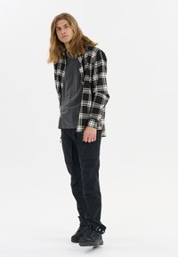 Flanellen shirt in zwart-wit geruit patroon, gedragen over een grijs T-shirt. Gecombineerd met zwarte cargo-broeken en zwarte wandelschoenen.