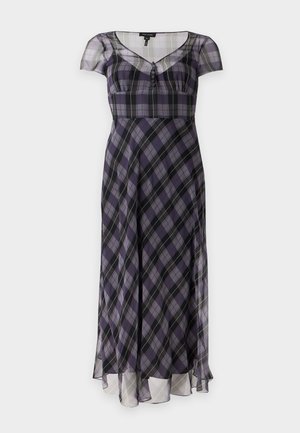 Mujer con un vestido midi de manga corta y transparente con un patrón de cuadros morados y negros y zapatos planos negros puntiagudos con detalles de lazo.