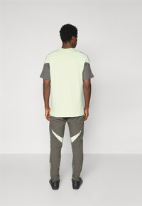 Light green short-sleeve shirt with dark gray accents, paired with gray pants featuring light green triangular patterns on the sides.