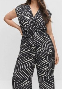 Jumpsuit de estampado en blanco y negro con escote en V, mangas cortas y cintura con cinturón. Presenta diseños en zigzag y un corte relajado.