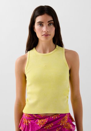 Top a righe giallo con scollatura rotonda e design senza maniche, abbinato a una gonna rosa con motivo floreale.