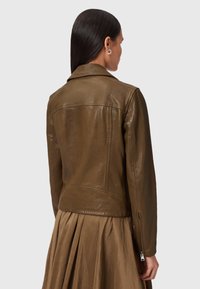 Giacca di pelle marrone con un design leggermente attillato, dotata di un colletto a punte, maniche con cerniera e una texture liscia e lucida.