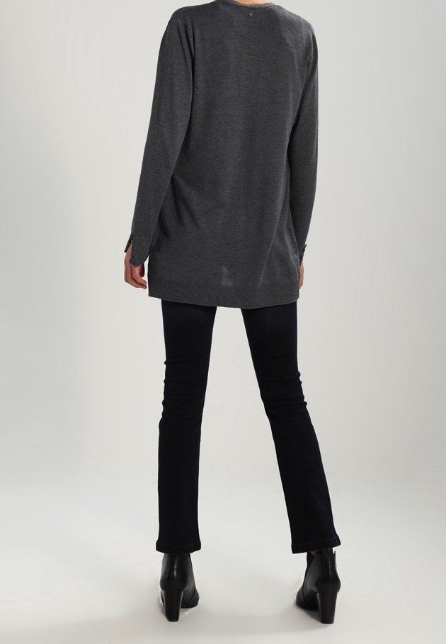 Lång grå stickad tröja med rundad halsringning, avslappnad passform och sidospjällsdetalj, kombinerad med svarta utsvängda jeans och ankelboots.
