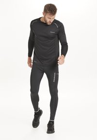 Schwarzes, sportliches Langarmshirt und eng anliegende Hose, aus dehnbarem Material gefertigt; mit reflektierenden Akzenten und Logo auf der Vorderseite.
