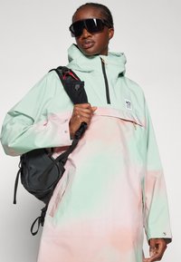 Lett, vannavstøtende jakke i mintgrønn og myk rosa gradient. Har hette, glidelåslomme og en avslappet passform.