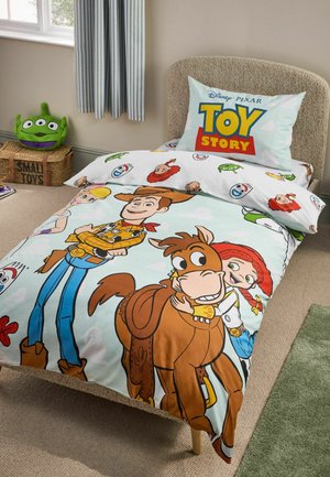 Cama individual con ropa de cama de Toy Story con Woody, Jessie y Bullseye, almohada con el logo de Toy Story y peluche de alienígena verde en una caja de almacenamiento cercana.