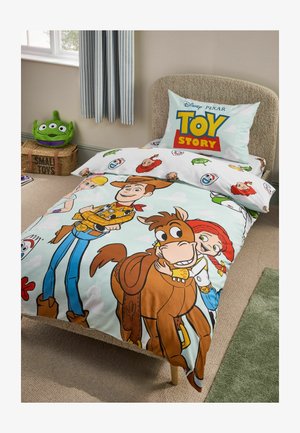 Łóżko pojedyncze z pościelą Toy Story z wizerunkami Woody’ego, Jessie i Bullseye’a, poduszka z logo Toy Story oraz zielony pluszowy kosmita na pobliskim pudełku do przechowywania.