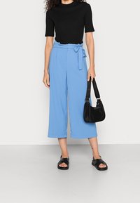 Ljusblå, vida byxor med knytbandsmidja, i kombination med en svart ribbad t-shirt och svarta slidesandaler. Svart axelväska.