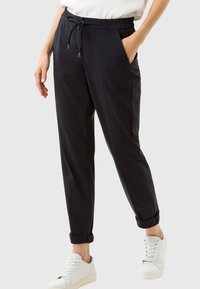 Czarne spodni z tapered, z elastycznym paskiem, bocznymi kieszeniami i podwiniętymi mankietami, wykonane z gładkiego materiału. Noszone z białymi trampkami.