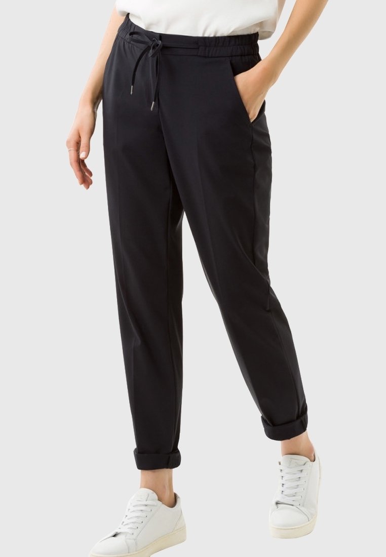 Czarne spodni z tapered, z elastycznym paskiem, bocznymi kieszeniami i podwiniętymi mankietami, wykonane z gładkiego materiału. Noszone z białymi trampkami.