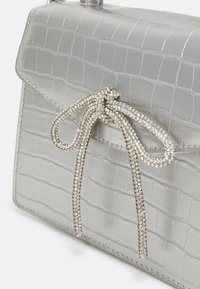 Sac en cuir d'alligator argenté avec un accent de nœud en strass étincelant, un design structuré et une texture lisse.