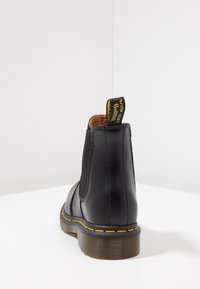 Black leather ankle boot with elastic side panels, yellow stitching, and a pull tab labeled "WITH SMILES BOUNDING." Textured rubber sole.
