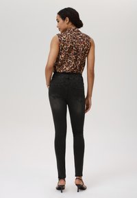 Top sin mangas de estampado de leopardo marrón combinado con jeans skinny negros de cintura alta y tacones negros con punta abierta, visto desde la parte de atrás.