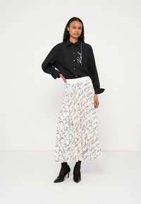 Μαύρο πουκάμισο με κουμπιά και μακριά μανίκια, συνδυασμένο με λευκή φούστα με μαύρο χειρόγραφο μοτίβο και μαύρες γόβες.