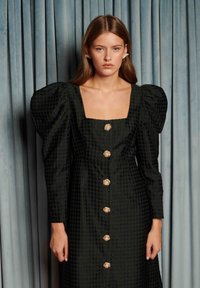 Grønn rutete kjole med puffede ermer, firkantet utringning og gullknapper med blomsterdekorasjoner. Glatt tekstur, knelang.